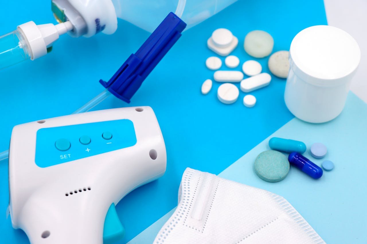 A collection of medical supplies including pills, a mask, and a thermometer on a blue surface.